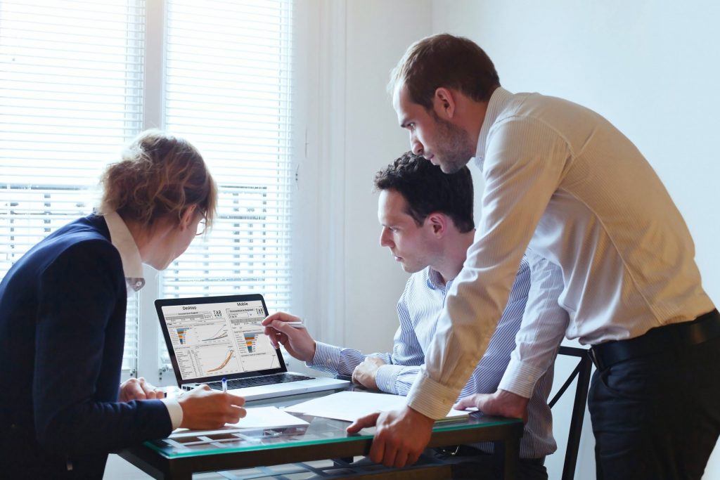 three people around a desk reviewing a tableau dashboard on a laptop
